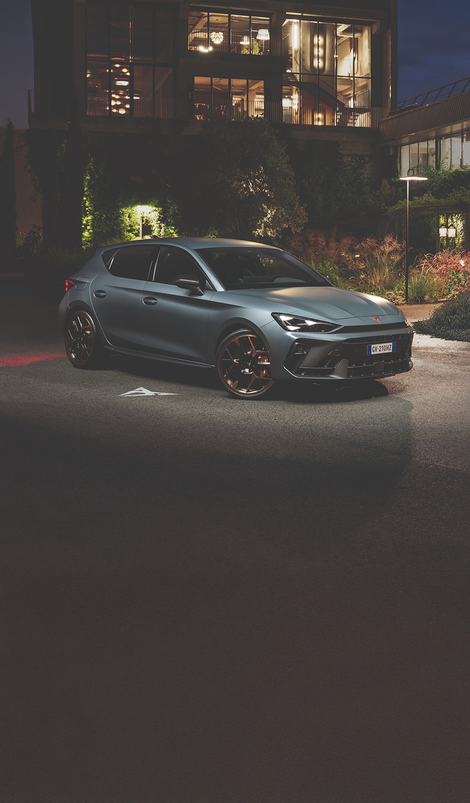 A dynamic scene featuring a CUPRA car in a sleek dark metallic color, positioned beside a blurred figure of a woman in a white dress using a VR headset and holding a conductor’s baton.  A dynamic scene featuring a CUPRA car in a sleek dark metallic color, positioned beside a blurred figure of a woman in a white dress using a VR headset and holding a conductor’s baton.