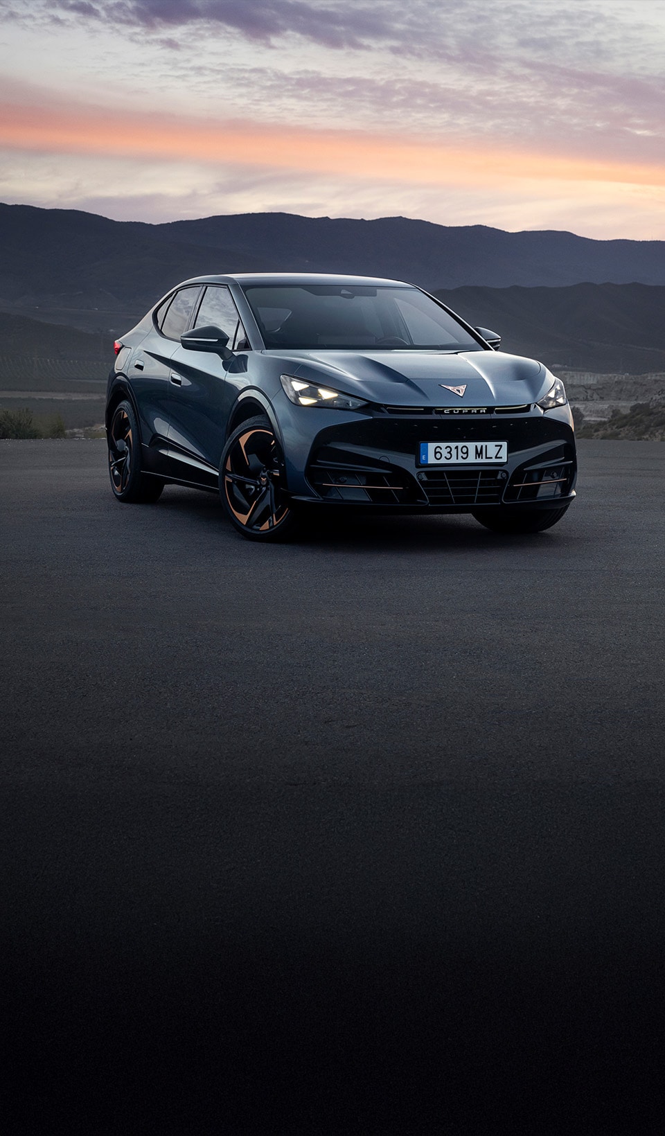 A CUPRA Leon hatchback seen from an elevated angle with its headlights on, next to a person covered in dark, flowing fabric that drapes onto the ground. A CUPRA Leon hatchback seen from an elevated angle with its headlights on, next to a person covered in dark, flowing fabric that drapes onto the ground.