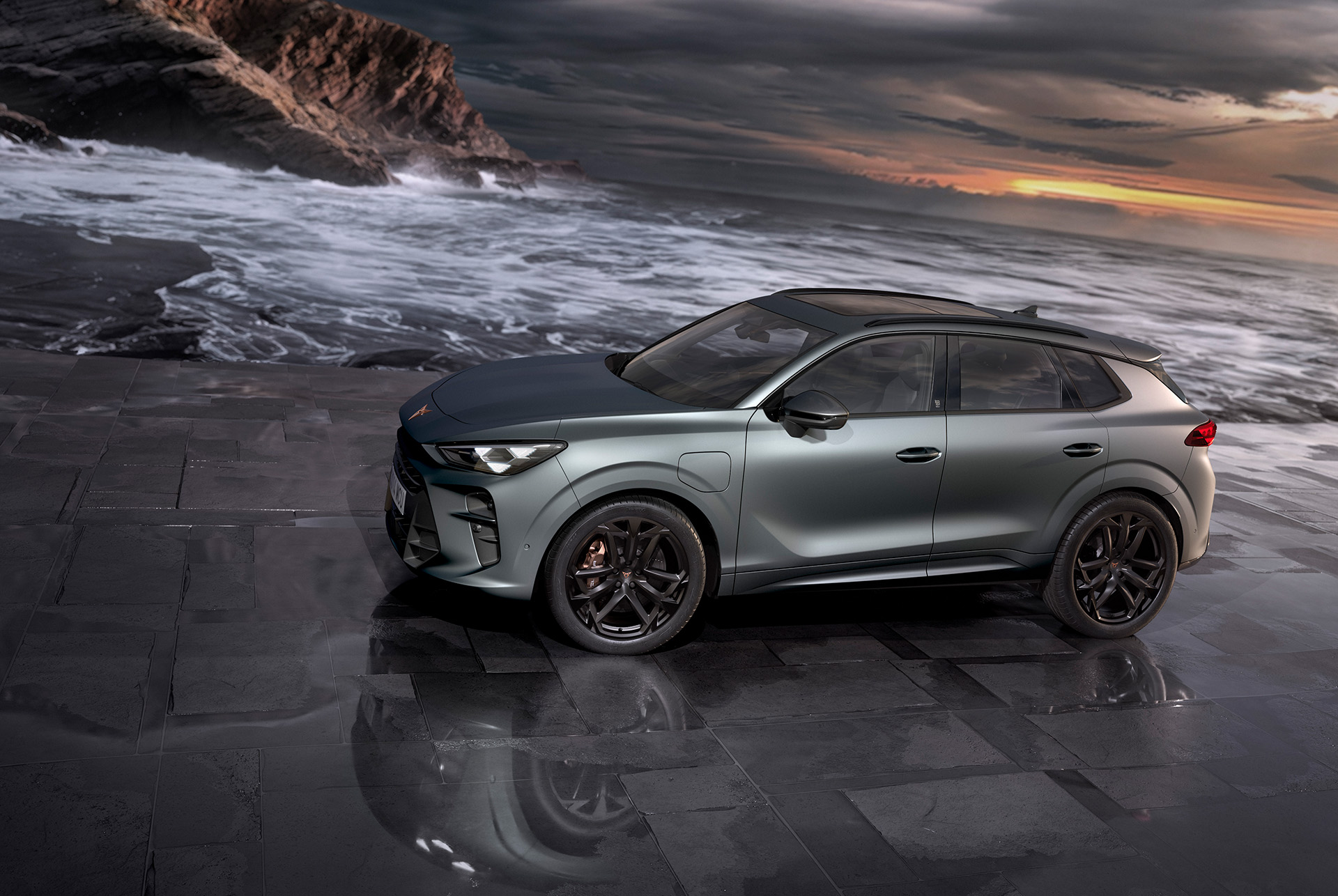 suv ibrido cupra terramar, nuovo modello 2024, fiancata, con cerchi in lega america's cup da 20 pollici e freni akebono, grigio enceladus opaco, sull’asfalto bagnato in riva al mare al tramonto. 